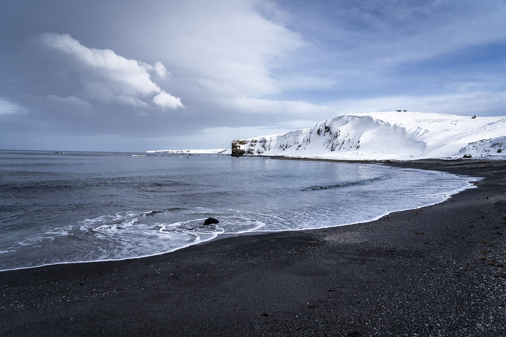 plage de sable noir falaises ciel bleu nuages Islande du Nord
